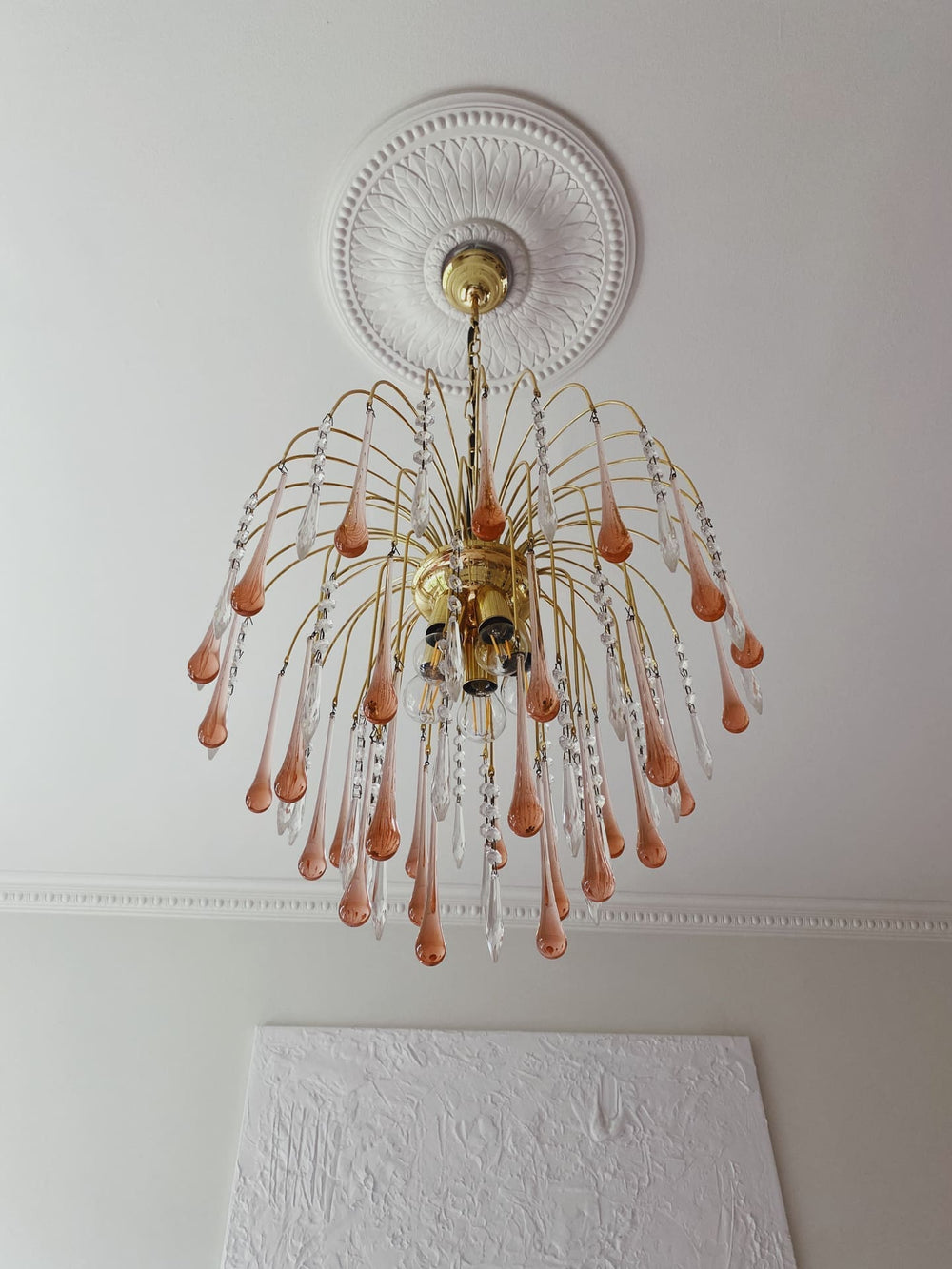 Gold chandelier with pink glass droplets hanging in a room.