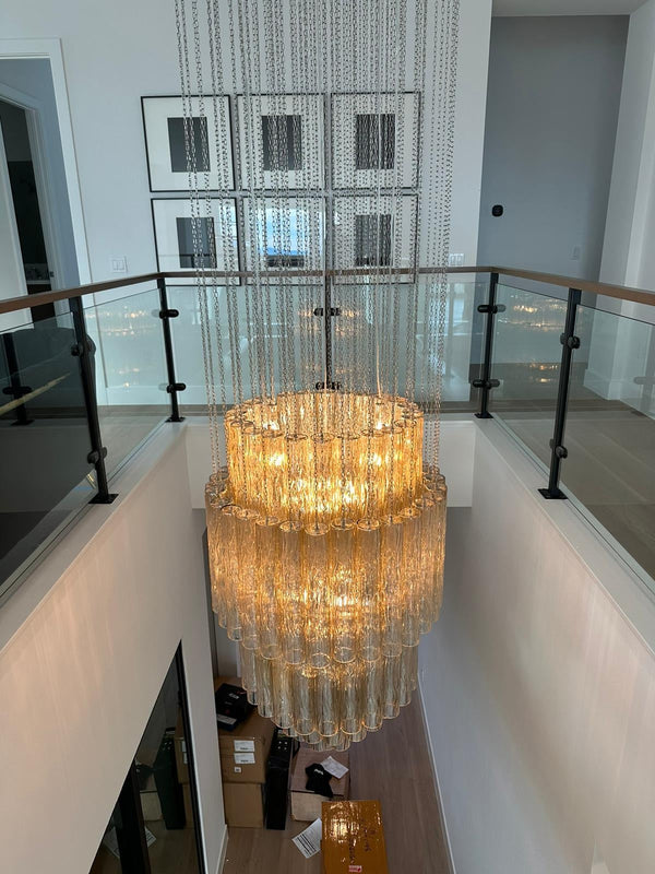 Large chandelier hanging in a modern indoor setting with glass panels and a staircase.
